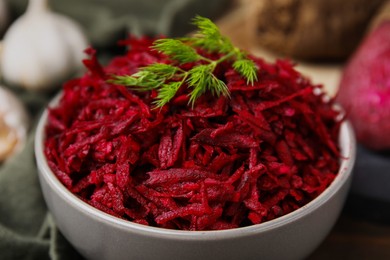 Grated red beet and dill in bowl on table, closeup