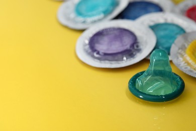Unpacked condom and packages on yellow background, closeup with space for text. Safe sex