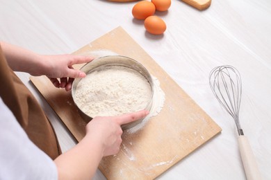 Photo of Woman sieving flour at white wooden table, above view