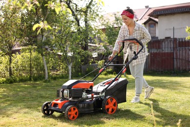 Photo of Smiling woman cutting green grass with lawn mower in garden