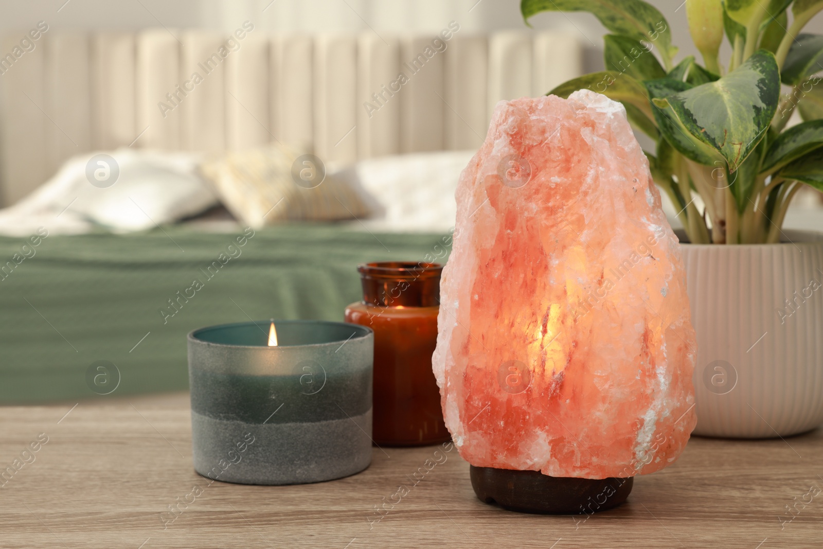 Photo of Beautiful Himalayan salt lamp, green plant and candles on wooden table in bedroom, space for text