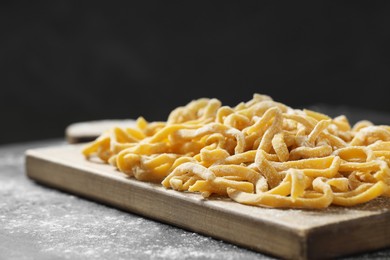Board with homemade pasta and flour on dark table, closeup. Space for text