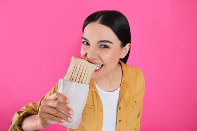Photo of Young woman eating delicious shawarma on pink background