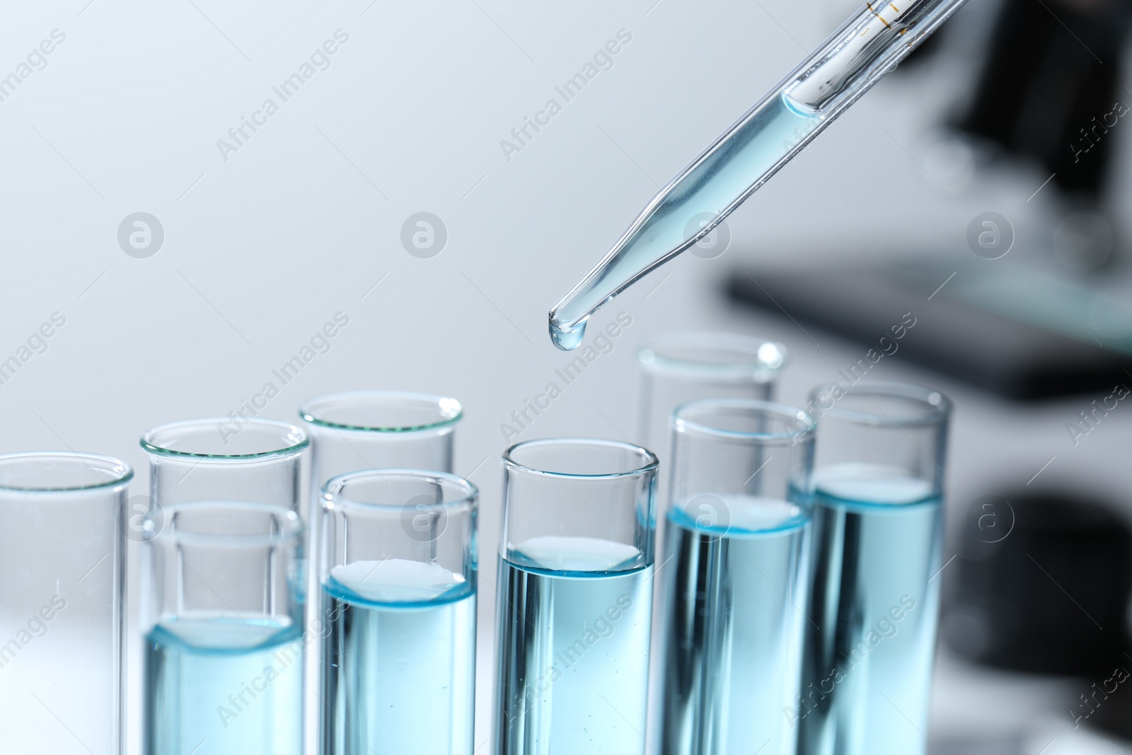 Photo of Dripping liquid from pipette into test tube on blurred background, closeup