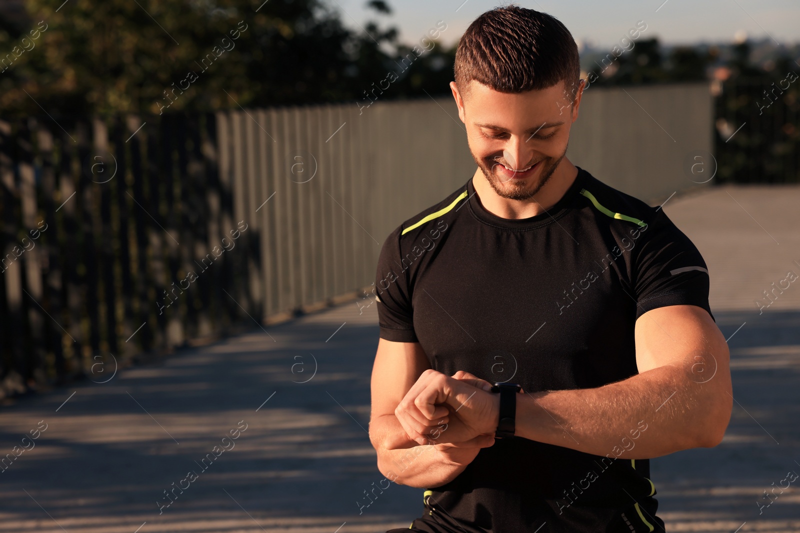 Photo of Attractive happy man checking pulse after training outdoors. Space for text