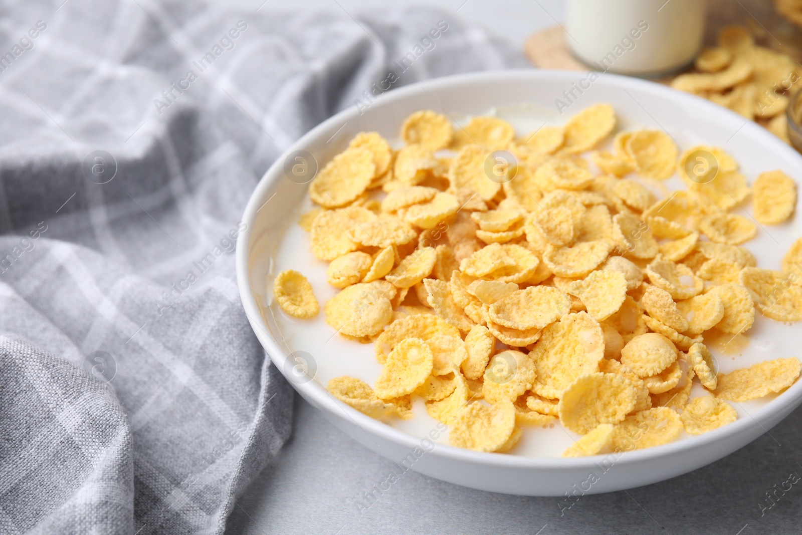 Photo of Breakfast cereal. Corn flakes and milk in bowl on light grey table, closeup