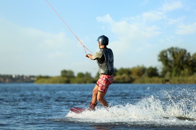 Photo of Teenage boy wakeboarding on river, back view. Extreme water sport