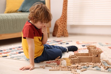 Little boy playing with wooden construction set on carpet in room, space for text. Child's toy