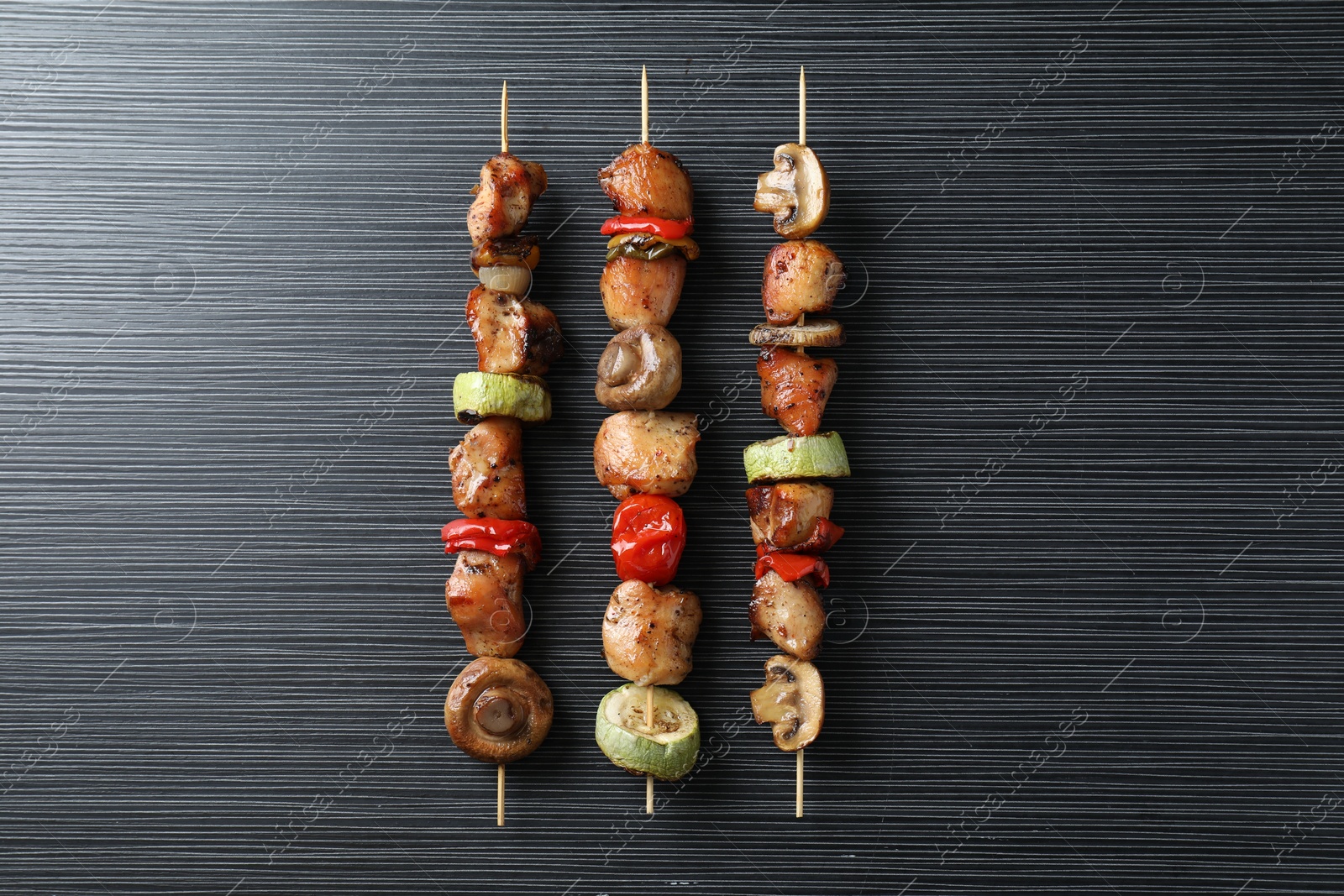 Photo of Delicious shish kebabs with vegetables on black table, top view