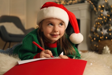 Cute child writing letter to Santa Claus while lying on floor at home. Christmas celebration