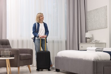 Photo of Smiling guest with suitcase exploring stylish hotel room