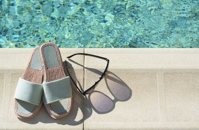 Photo of Stylish sunglasses and slippers at poolside on sunny day, space for text. Beach accessories