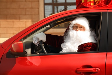 Photo of Authentic Santa Claus with bag full of presents on roof driving modern car, outdoors
