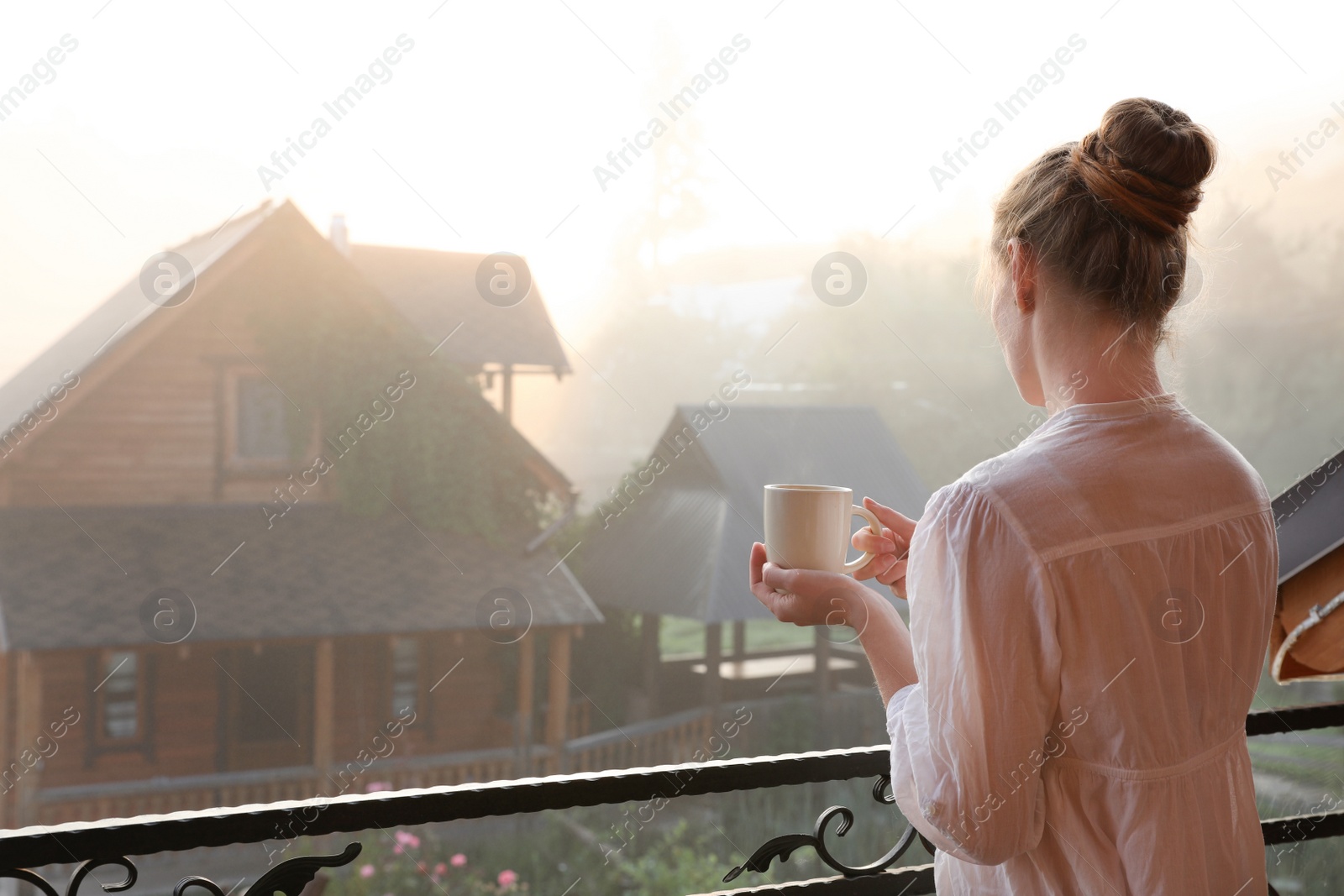 Photo of Young woman with cup of tea standing on balcony in morning