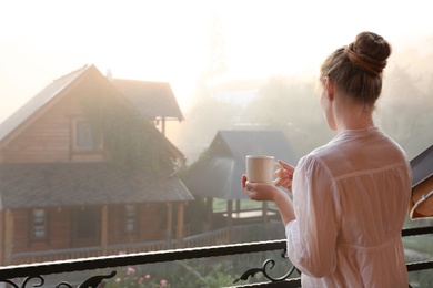 Young woman with cup of tea standing on balcony in morning