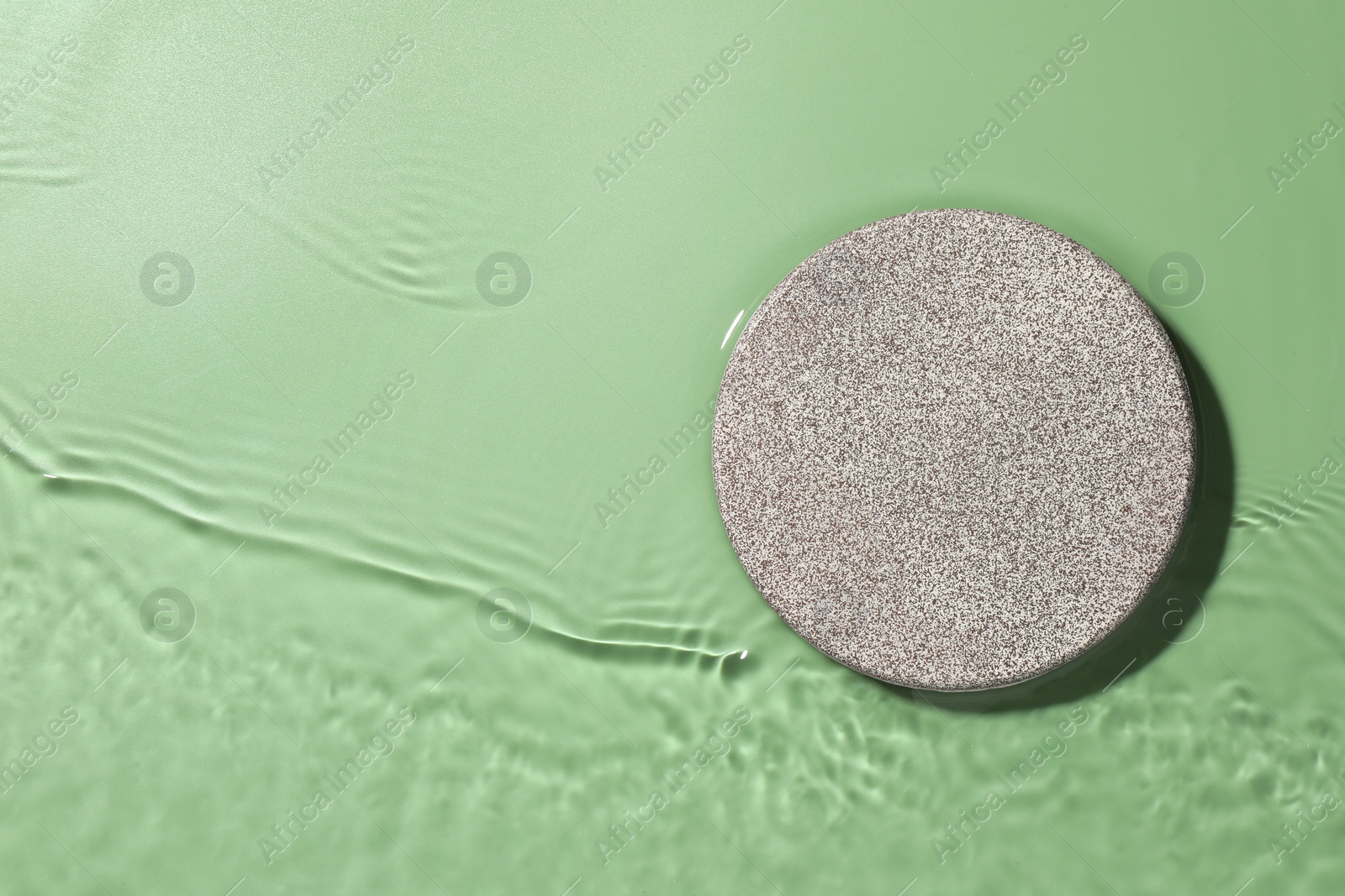 Photo of Presentation of product. Stone podium in water on green background, top view. Space for text