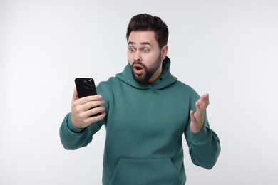 Shocked young man using smartphone on white background