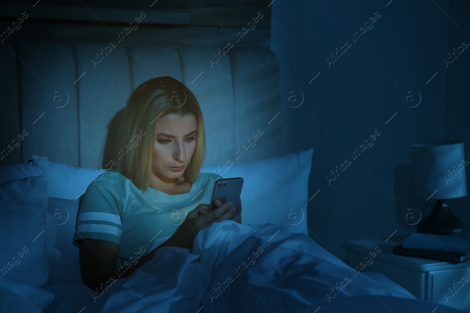 Photo of Young woman using smartphone in bed at night. Nomophobia and sleeping disorder problem