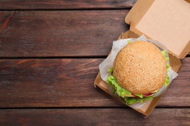Photo of Delicious burger in cardboard box on wooden table, top view. Space for text