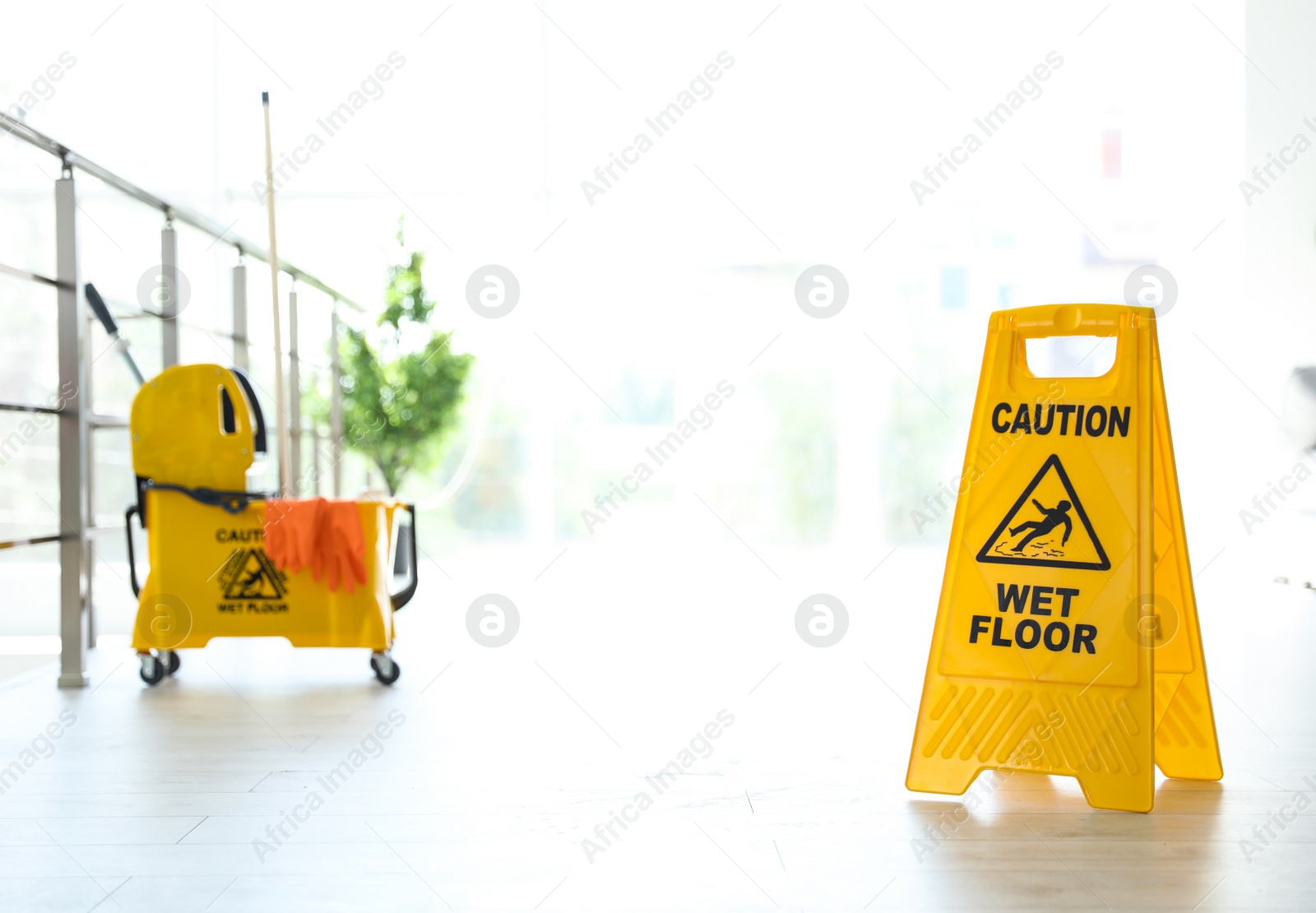 Photo of Phrase "CAUTION WET FLOOR" on safety sign and mop bucket with cleaning supplies, indoors