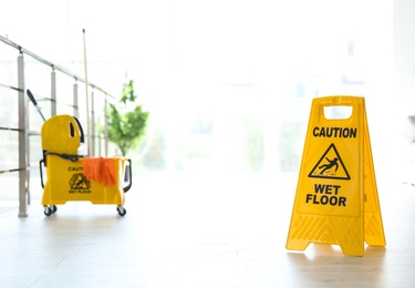 Phrase "CAUTION WET FLOOR" on safety sign and mop bucket with cleaning supplies, indoors