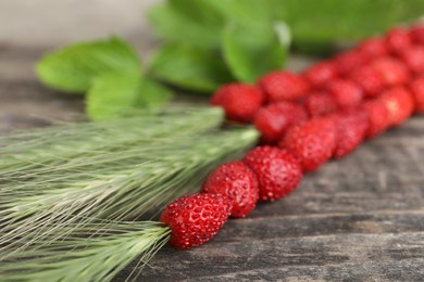 Photo of Grass stems with wild strawberries on wooden table, closeup