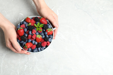 Photo of Woman with bowl of delicious berries at light table, closeup. Space for text