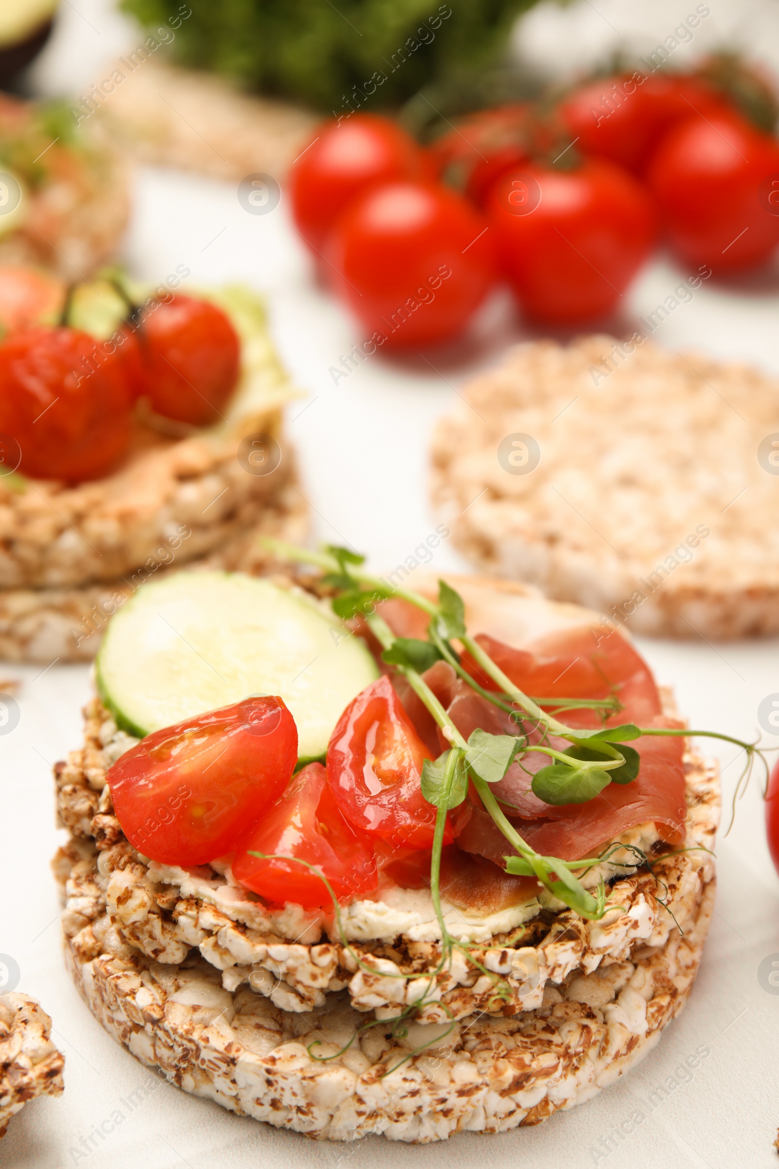 Photo of Crunchy buckwheat cakes with prosciutto, tomatoes and cucumber slice on white table, closeup