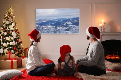 Family watching TV in room decorated for Christmas