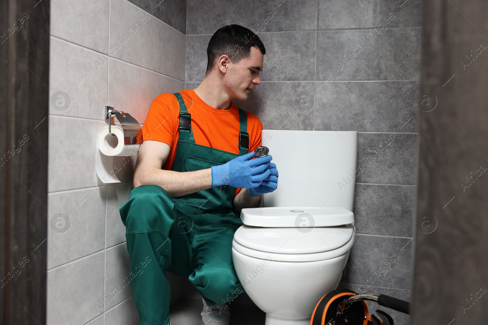 Photo of Young plumber repairing toilet bowl in water closet