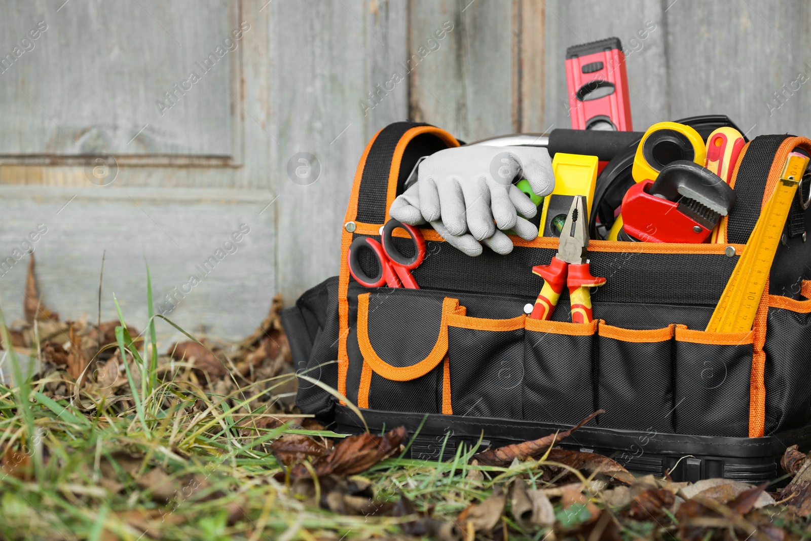 Photo of Bag with different tools for repair on grass near wooden door outdoors, space for text