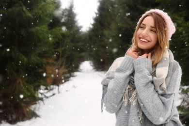 Young woman in snowy conifer forest, space for text. Winter vacation