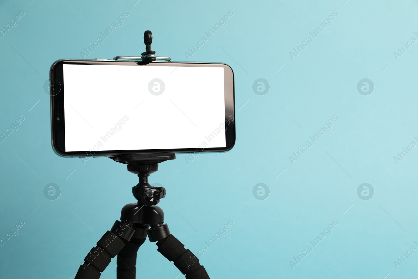 Photo of Modern tripod with smartphone on turquoise background. Space for text