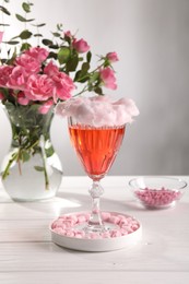 Cotton candy cocktail in glass, marshmallows and vase with pink roses on white wooden table against gray background