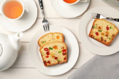 Photo of Delicious cake with candied fruits and tea on white wooden table, flat lay