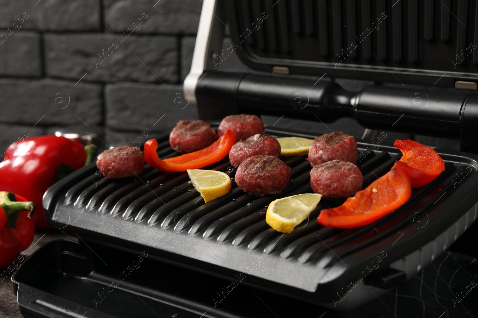 Photo of Electric grill with meat balls, bell pepper and lemon on table, closeup