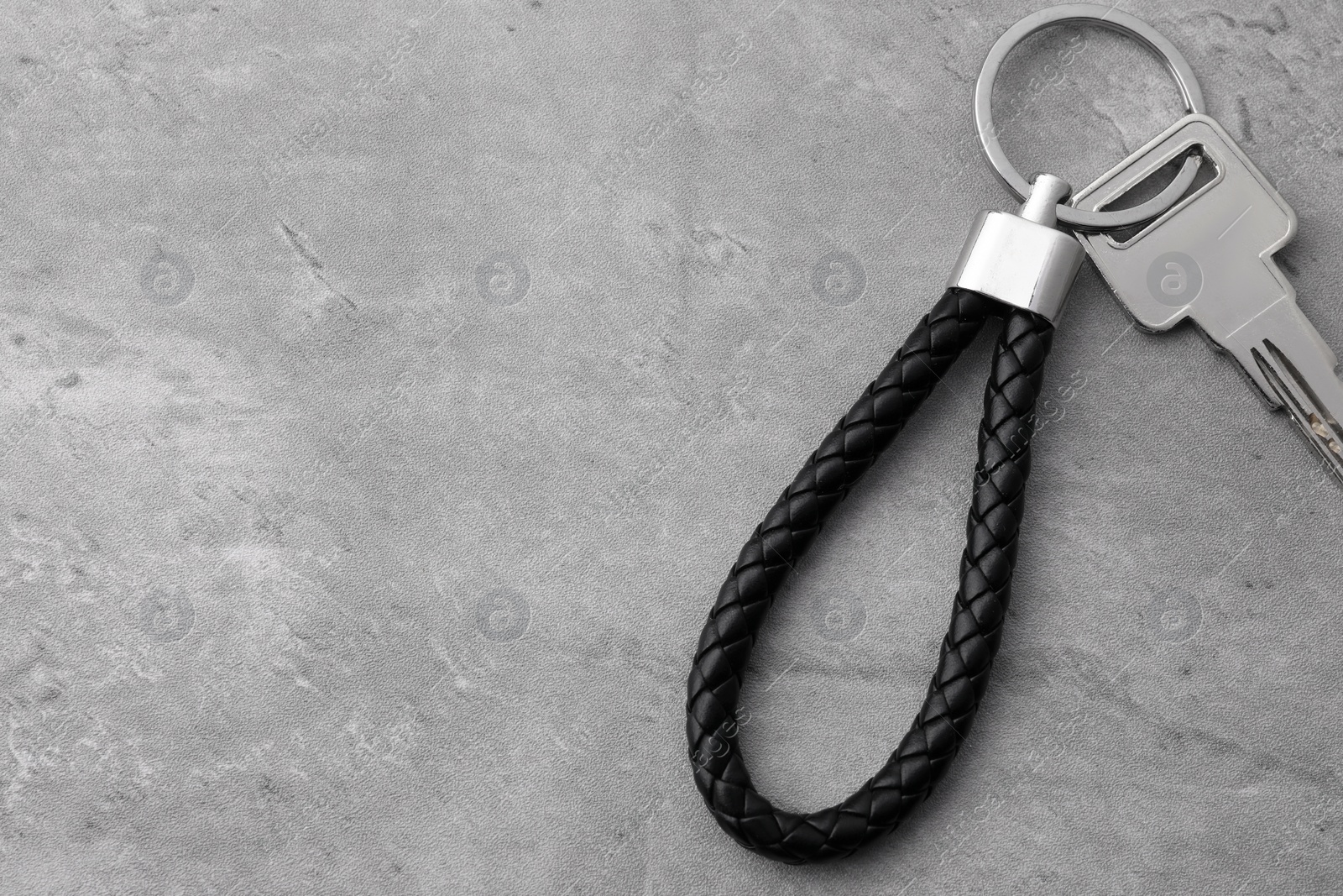 Photo of Key with black leather keychain on grey background, top view. Space for text