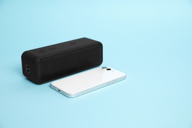 Photo of Portable bluetooth speaker and smartphone on light blue background, space for text. Audio equipment