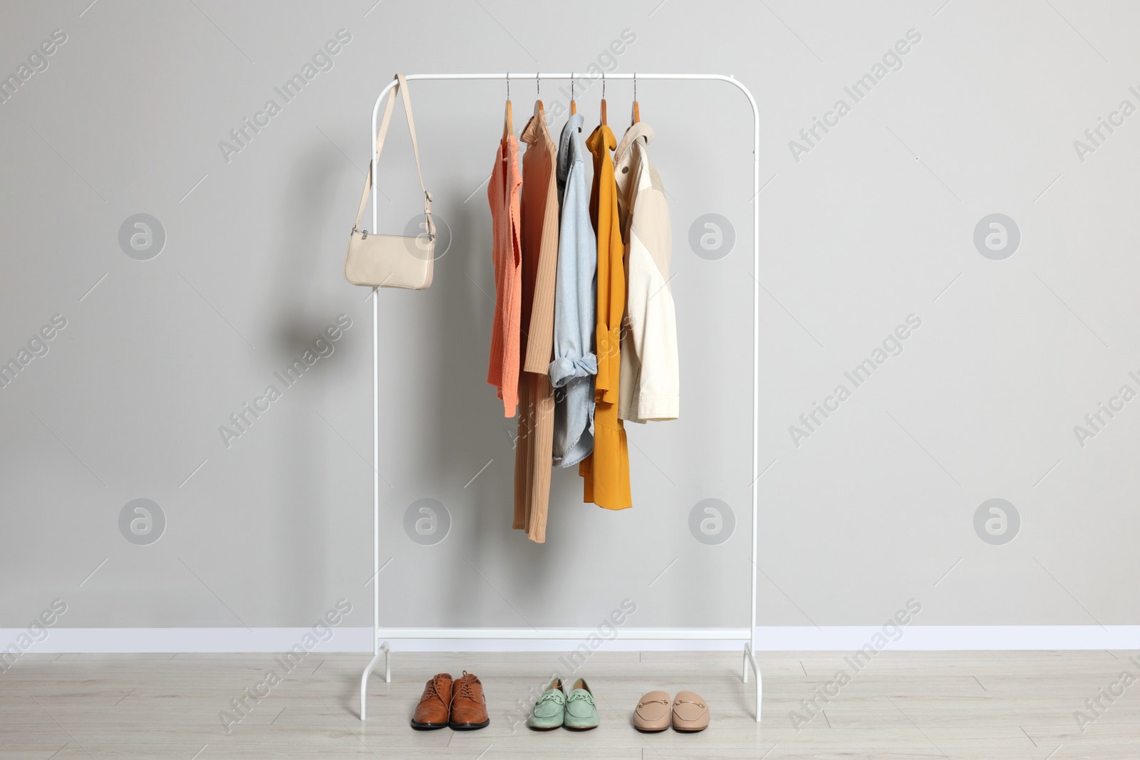Photo of Rack with stylish women's clothes on wooden hangers, bag and shoes near light grey wall