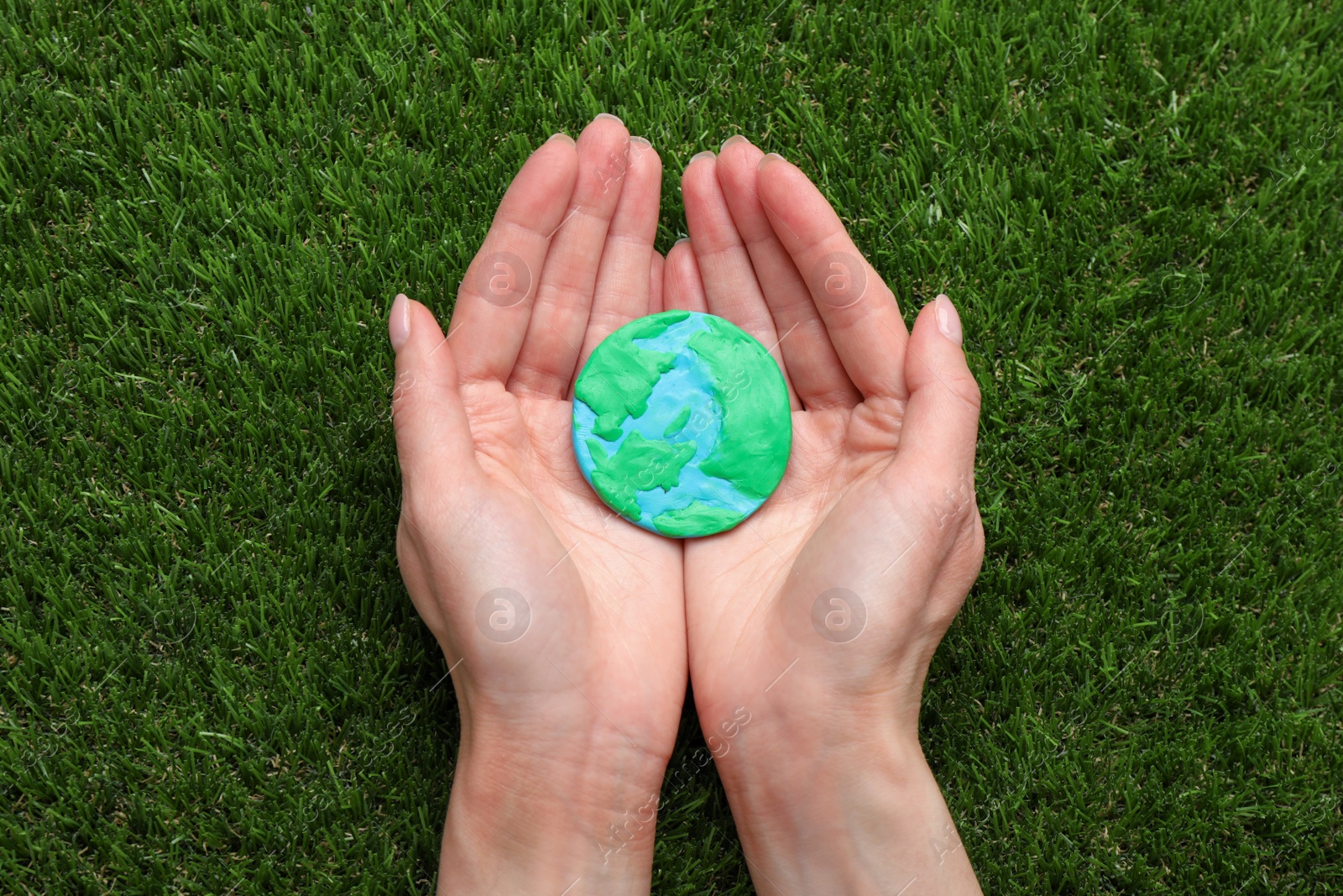 Photo of Happy Earth Day. Woman with plasticine planet on green grass, top view