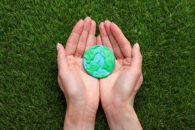 Photo of Happy Earth Day. Woman with plasticine planet on green grass, top view