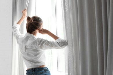 Photo of Young happy woman near window at home. Lazy morning