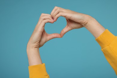 Photo of Man showing heart gesture with hands on light blue background, closeup