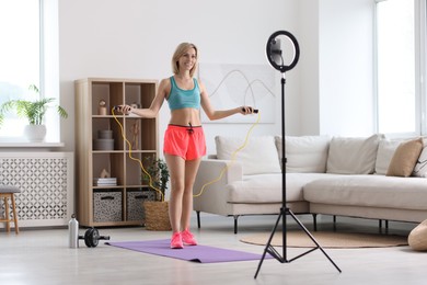 Photo of Smiling sports blogger jumping with rope while streaming online fitness lesson with smartphone at home