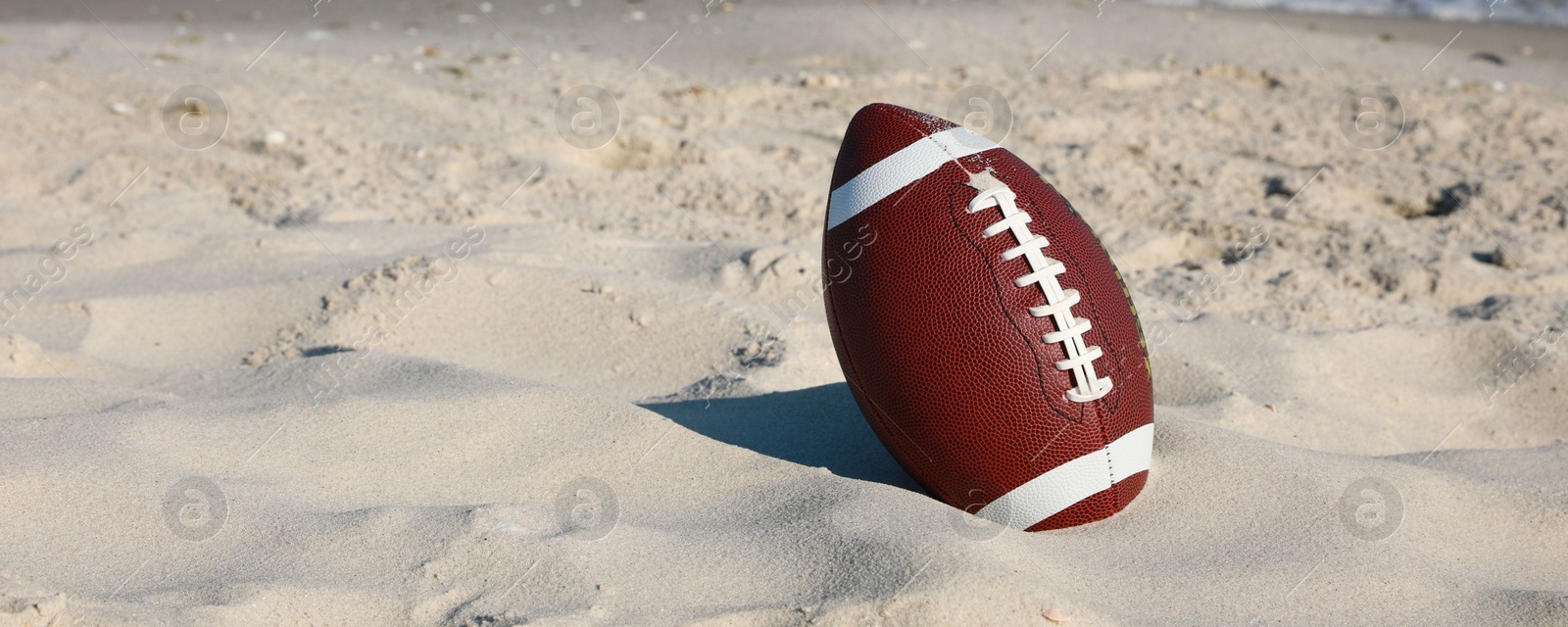 Photo of American football ball on beach. Space for text