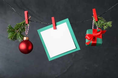 Photo of Blank Christmas card and festive decor on rope against black background, space for text