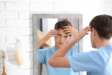 Photo of Teenage boy with acne problem looking in mirror at home