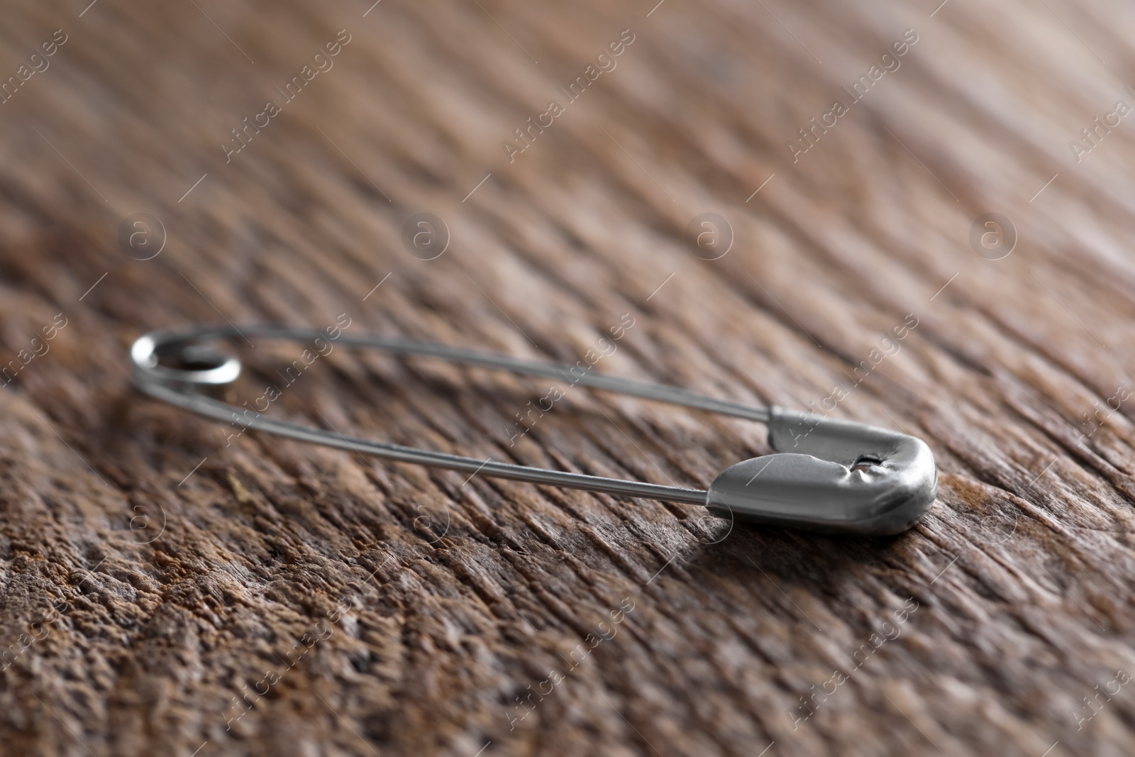 Photo of New safety pin on wooden table, closeup