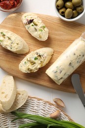 Photo of Tasty butter with green onion, olives, garlic and bread on white wooden table, top view