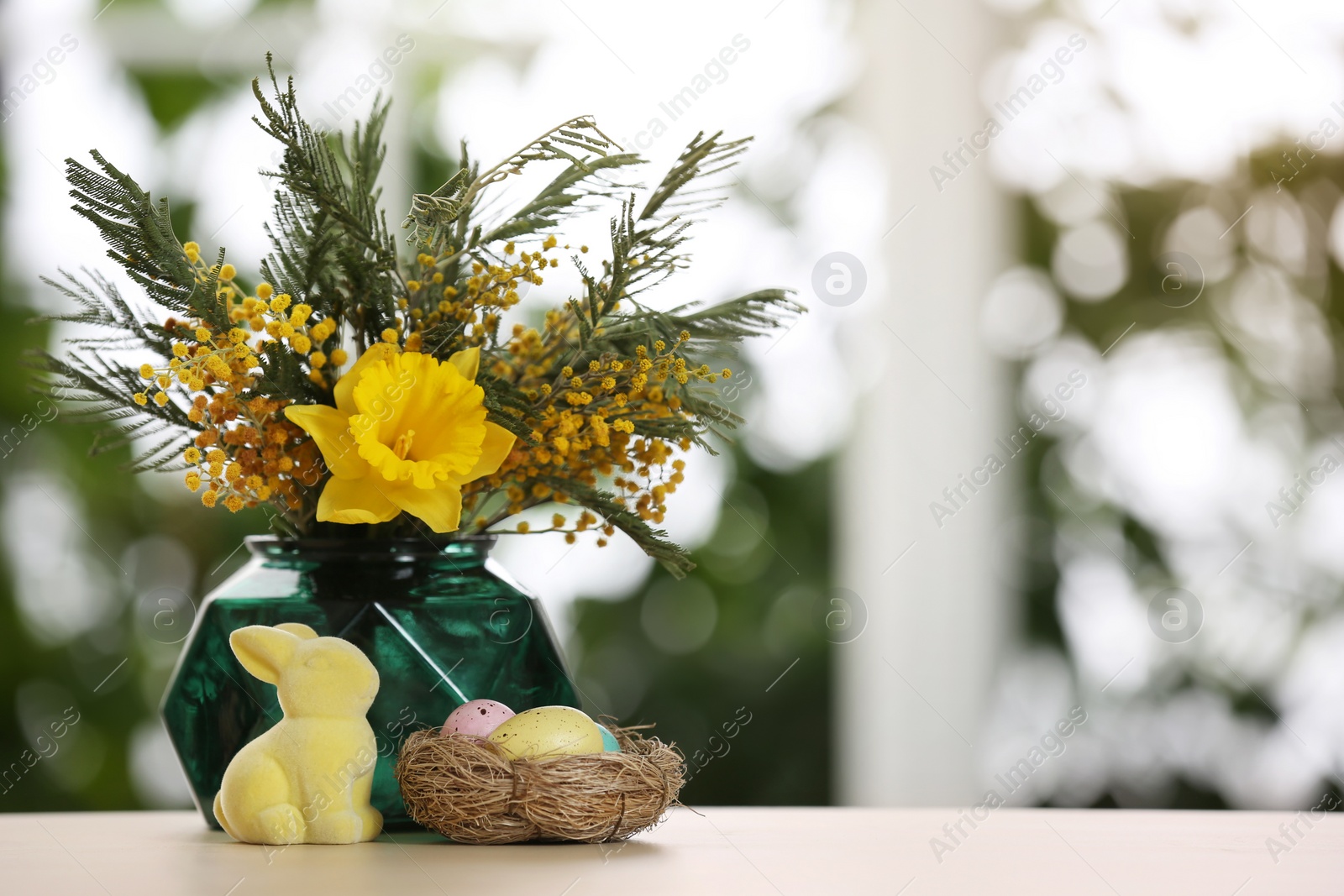 Photo of Festive composition with Easter eggs in decorative nest on table against blurred window, space for text